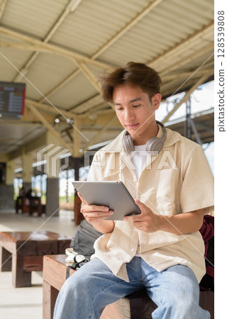 Young non binary tourist traveler in train station using digital tablet computer Young non binary tourist traveler in train station using digital tablet computer 128539808