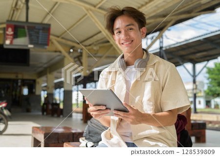 Young non binary tourist traveler in train station using digital tablet computer 128539809
