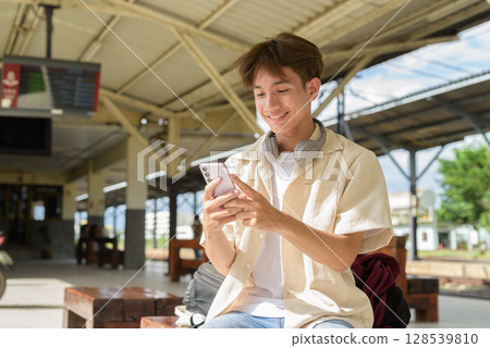 Young non binary tourist traveler in train station using mobile phone 128539810