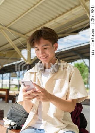 Young non binary tourist traveler in train station using mobile phone 128539813