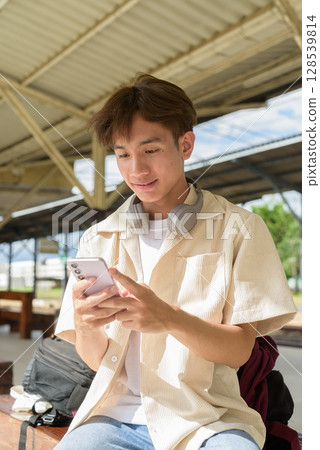 Young non binary tourist traveler in train station using mobile phone Young non binary tourist traveler in train station using mobile phone 128539814