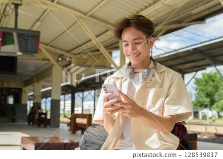 Young non binary tourist traveler in train station using mobile phone 128539817