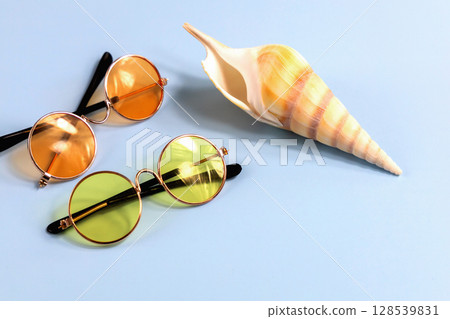 Large sea shell and sunglasses on blue background Large sea shell and sunglasses on blue background 128539831