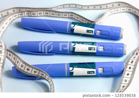 Three Ozempic syringe drug pen and measuring tape on blue 128539838