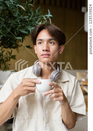 Non binary Asian student man sitting in modern cafe drinking coffee 128539924