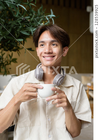 Non binary Asian student man sitting in modern cafe drinking coffee 128539925