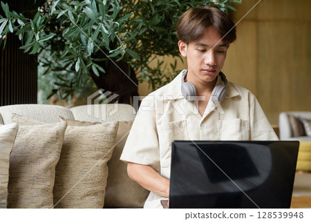 Non binary Asian student man sitting in modern coffee shop using laptop computer Non binary Asian student man sitting in modern coffee shop using laptop computer 128539948