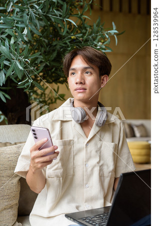 Non binary Asian student man sitting in modern coffee shop using laptop computer 128539964
