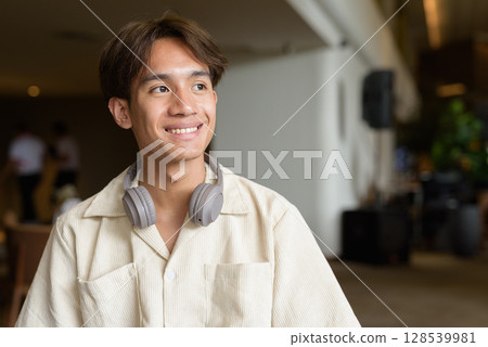 Non binary Asian student man sitting in modern coffee shop 128539981