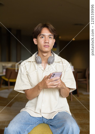 Non binary Asian student man sitting in modern coffee shop using phone Non binary Asian student man sitting in modern coffee shop using phone 128539996