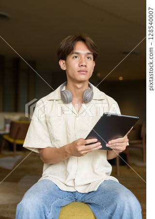 Non binary Asian student man sitting in modern coffee shop using digital tablet computer 128540007