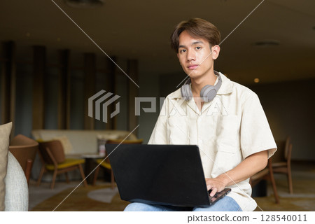 Non binary Asian student man sitting in modern coffee shop using laptop computer Non binary Asian student man sitting in modern coffee shop using laptop computer 128540011