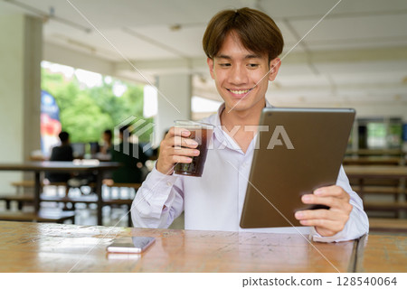 Non binary university student sitting in college campus using tablet computer 128540064