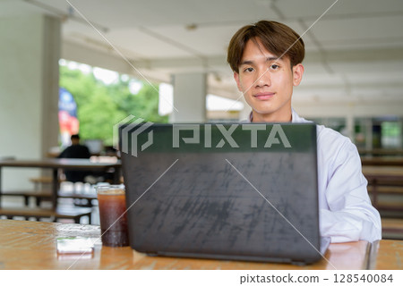 Non binary university student sitting in college campus using laptop computer Non binary university student sitting in college campus using laptop computer 128540084
