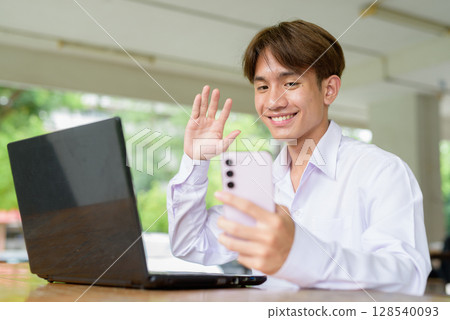 Non binary university student sitting in college campus using laptop computer and phone Non binary university student sitting in college campus using laptop computer and phone 128540093