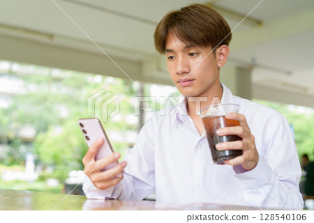 Non binary university student sitting in college campus Non binary university student sitting in college campus 128540106