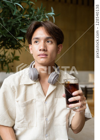 Non binary Asian student man sitting in modern coffee shop drinking cola 128540138