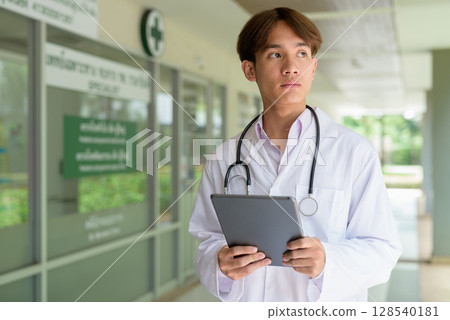 Young healthcare worker wearing lab coat in front of medical clinic using tablet computer 128540181