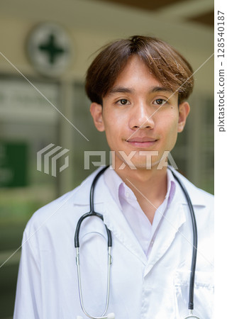 Young healthcare worker wearing lab coat in front of medical clinic 128540187