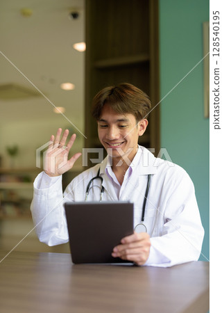 Young healthcare worker wearing lab coat sitting inside clinic library Young healthcare worker wearing lab coat sitting inside clinic library 128540195
