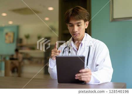 Young healthcare worker wearing lab coat sitting inside clinic library Young healthcare worker wearing lab coat sitting inside clinic library 128540196