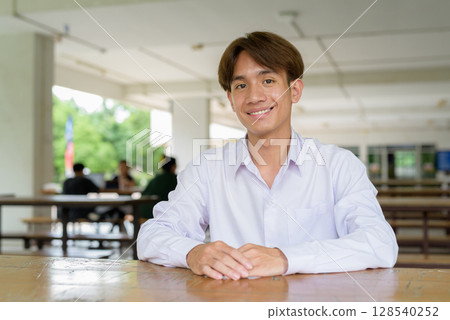Non binary university student sitting and smiling in college campus 128540252