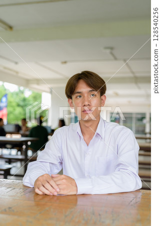 Non binary university student sitting in college campus 128540256