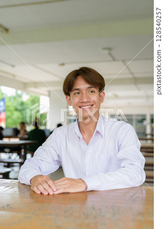 Non binary university student sitting and smiling in college campus Non binary university student sitting and smiling in college campus 128540257