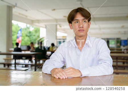 Non binary university student sitting in college campus Non binary university student sitting in college campus 128540258