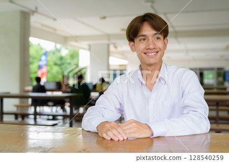 Non binary university student sitting in college campus 128540259