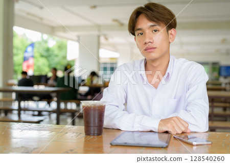 Non binary university student sitting in college campus 128540260