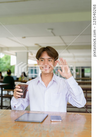 Non binary university student sitting in college campus using phone 128540268