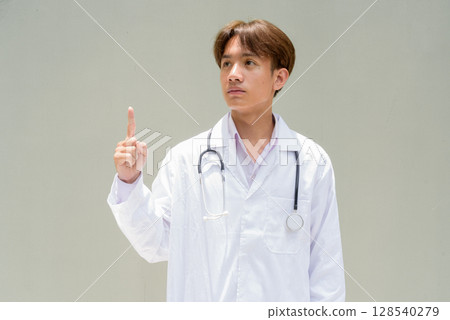 Young healthcare worker wearing lab coat pointing finger 128540279