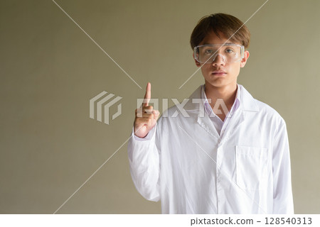 Young scientist student researcher wearing lab coat pointing finger up 128540313