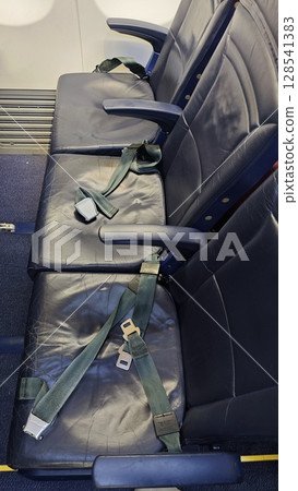 Seats on an aircraft with safety belts displayed in a quiet cabin during daytime travel 128541383