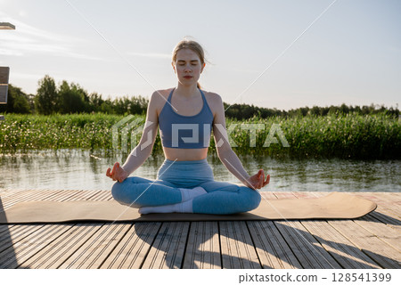 Young woman practicing yoga pose on wooden dock near lake in summer morning light Young woman practicing yoga pose on wooden dock near lake in summer morning light 128541399