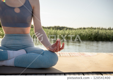 close-up of woman's hand in meditation mudra during yoga on wooden dock near lake in summer morning close-up of woman's hand in meditation mudra during yoga on wooden dock near lake in summer morning 128541400