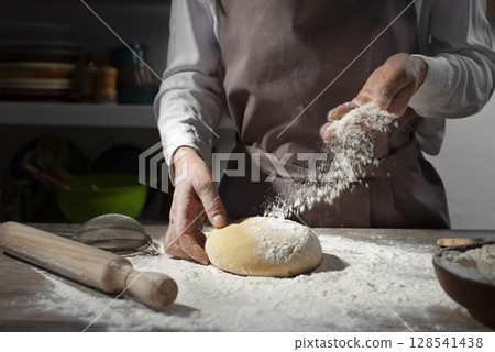 Baking concept. Caucasian female hands throwing flour at the dough. Baking concept. Caucasian female hands throwing flour at the dough. 128541438