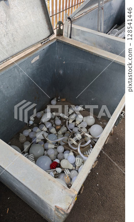 Old and discarded light bulbs collected in a large storage box at a recycling center during the afternoon sunlight 128541446