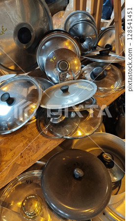Piled collection of gleaming pot lids in a cozy workshop capturing the essence of culinary creativity and home cooking heritage 128541451
