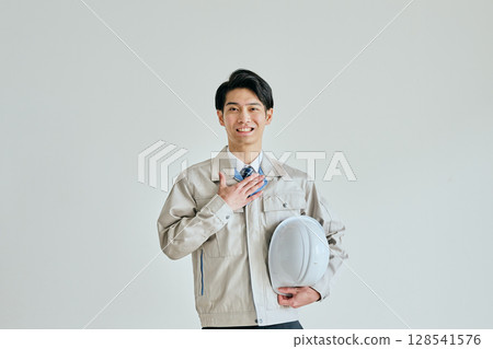 A young man in work clothes holding his hand on his chest 128541576