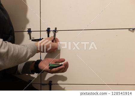 Man Installing Tile Leveling System Components. Man tiling the walls. 128541914