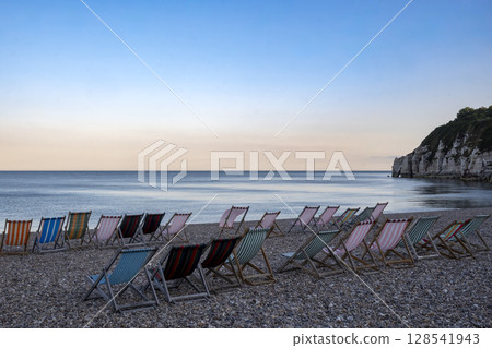 Line of deckchairs in calm bay on south coast of England 128541943