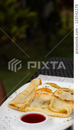 A crepe with an egg served on a white plate with red sauce for breakfast in an outdoor setting showing the candid moment of morning spring 128542276