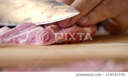 Close up of chef Butcher cutting pork meat with knife on kitchen, cooking food. The chef butcher preparing pork meat for cooking. 128542330