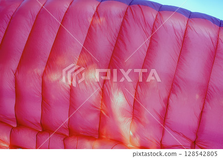 Close-up of pink paraglider wing. Bright pink paraglider wing fills frame with sun reflections highlighting texture and fabric. Concept of sport equipment, vibrant color background 128542805