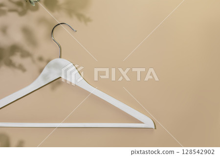 Sustainable shopping, buying or sales concept. Eco friendly still life with white wooden hanger on beige background with plant shadows. Flat lay, copy space Sustainable shopping, buying or sales concept. Eco friendly still life with white wooden hanger on beige background with plant shadows. Flat lay, copy space 128542902
