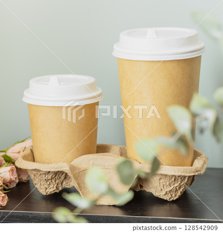 Spring romantic eco friendly card with two disposable cardboard cups with coffee on wooden table on blue background with eucalyptus branch. Dating or love concept. Coffee to go. Morning still life 128542909