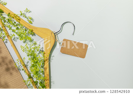 Sustainable, ecological shopping, buying or sales concept. Eco friendly still life with wooden hanger with green branches and empty label on blue background with plant shadows. Flat lay, copy space Sustainable, ecological shopping, buying or sales concept. Eco friendly still life with wooden hanger with green branches and empty label on blue background with plant shadows. Flat lay, copy space 128542910