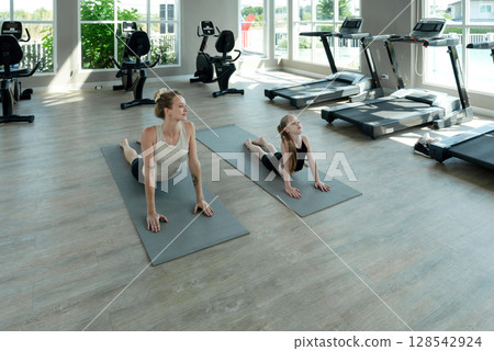 Girl in sportswear practice yoga with her mother in fitness center. Warm up and cool down stretching before and after exercises help reduce muscle pain. 128542924